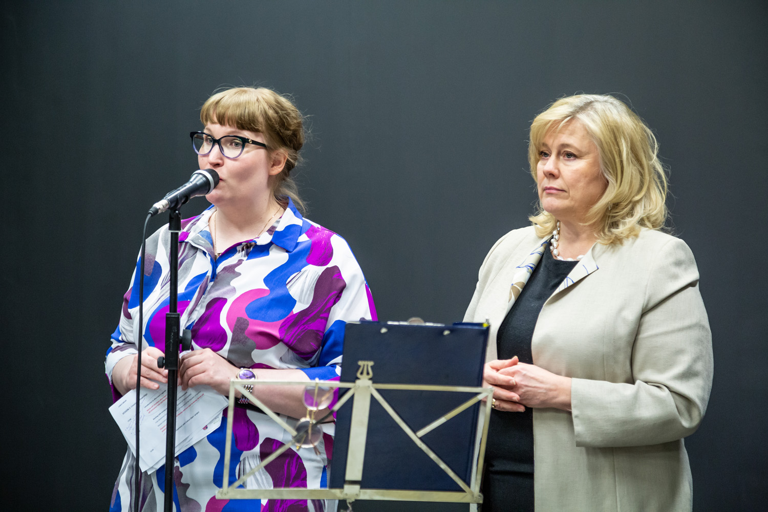 Project Coordinator and Director of Culture stand side by side in front of a microphone